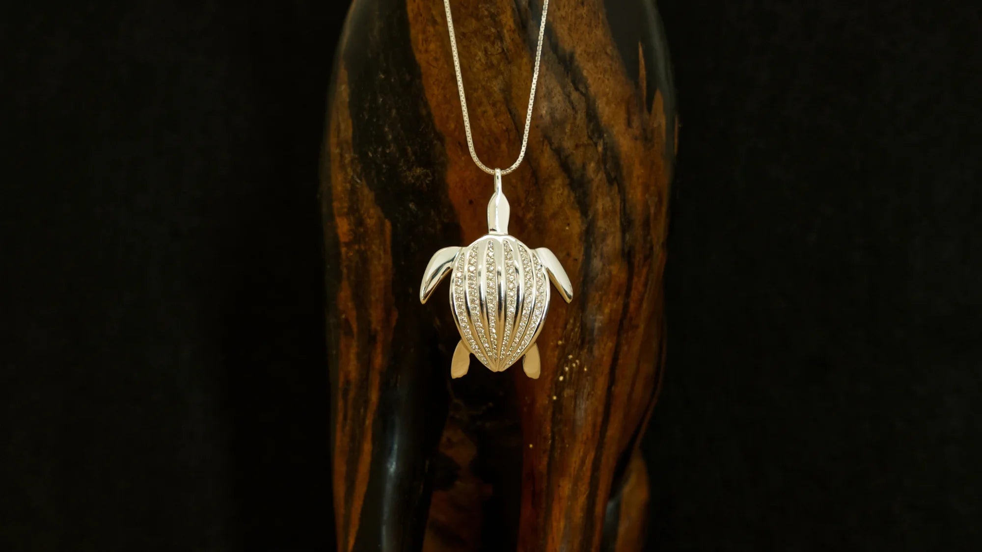 Le pendentif Totem Luth suspendu devant une pièce de bois sombre, de la collection Totem Luth | Honu
