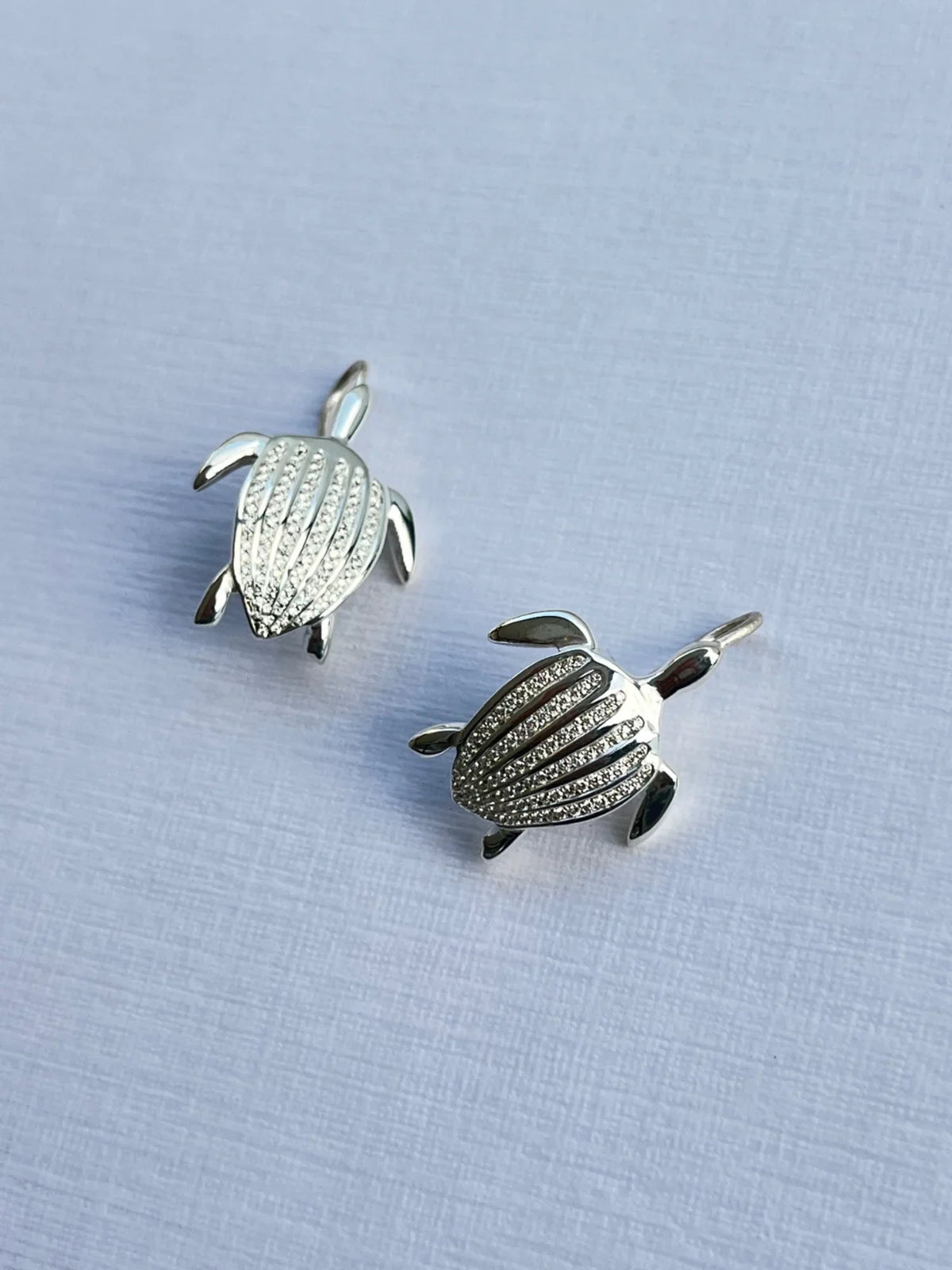 Les boucles d'oreilles Totem Luth, diamants incolores sur argent massif, la paire posée en biais, les sept carènes détaillées | Honu