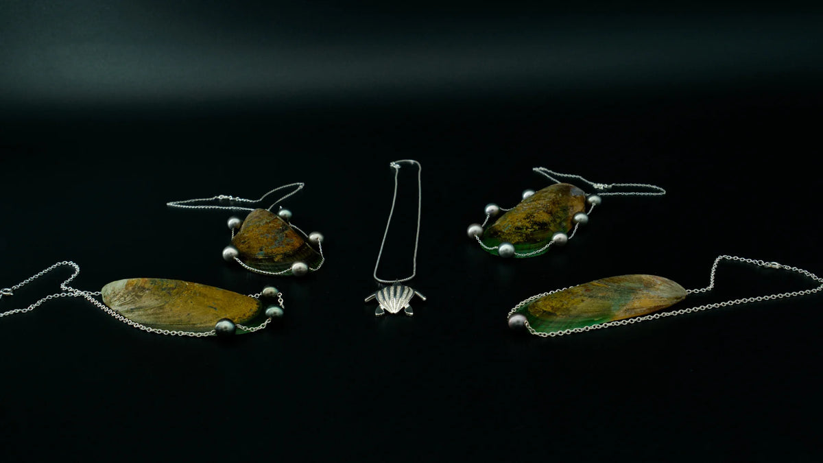 Les colliers de la collection Instinct disposés sur des coquillages autour d'un pendentif tortue Luth, plan large | Honu