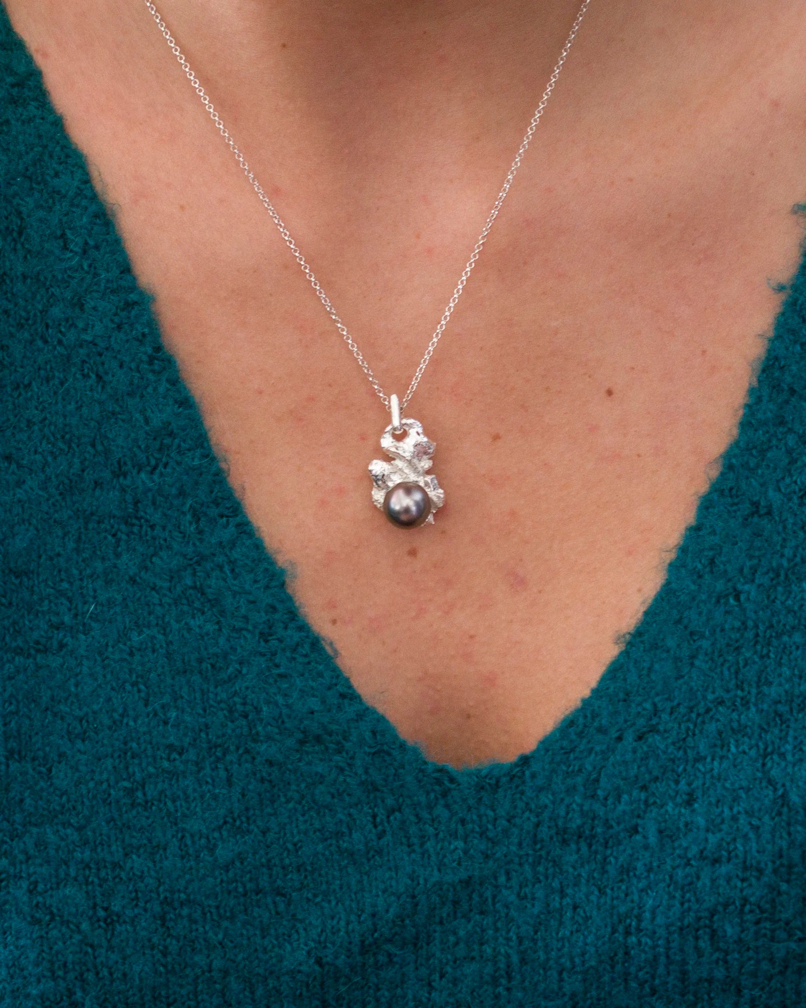 Collier avec pendentif artisanal en argent massif 950 et perle de Tahiti foncée, porté sur un pull bleu-vert.