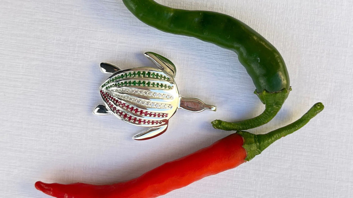 Le pendentif Totem Luth Italia, tsavorites, diamants et rubis sur argent massif, à l'horizontale entre piments vert et rouge, format panoramique | Honu