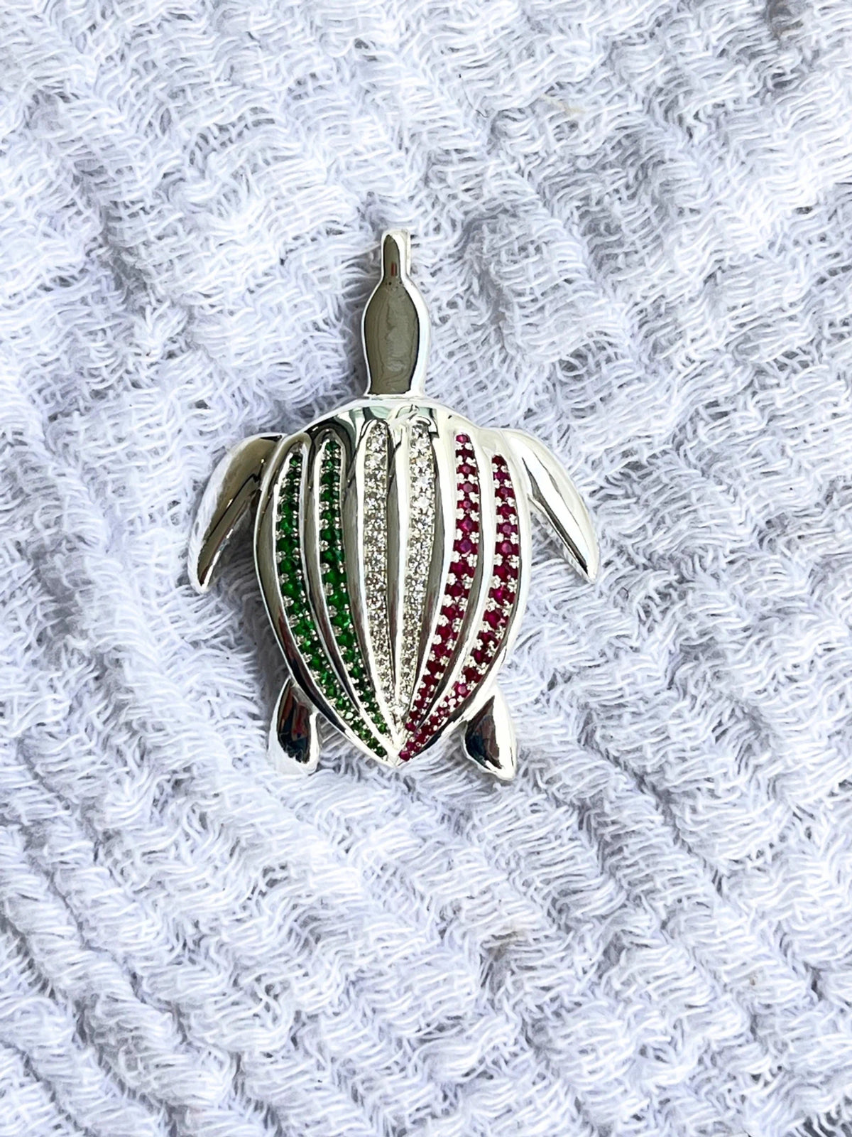 Le pendentif Totem Luth Italia, tsavorites, diamants et rubis sur argent massif, en gros plan sur un tissu éponge blanc | Honu
