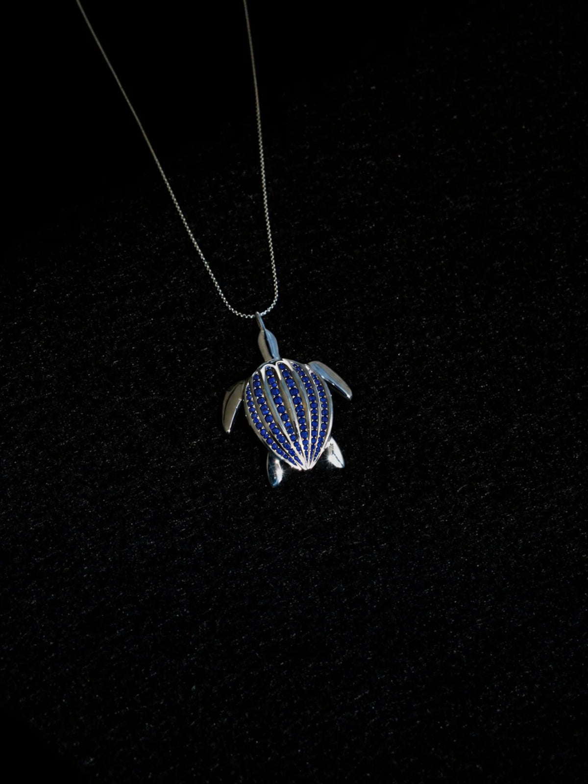 Le pendentif Totem Luth, saphirs bleus sur argent massif, sur velours noir, lumière rasante sur le pavage | Honu