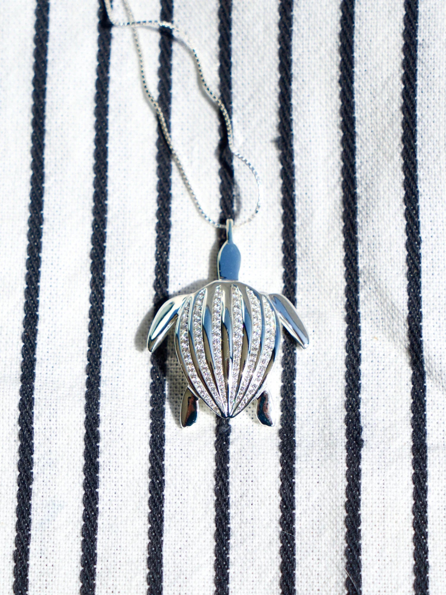 Le pendentif Totem Luth posé sur un tissu rayé, sa chaîne déployée, de la collection Totem Luth | Honu