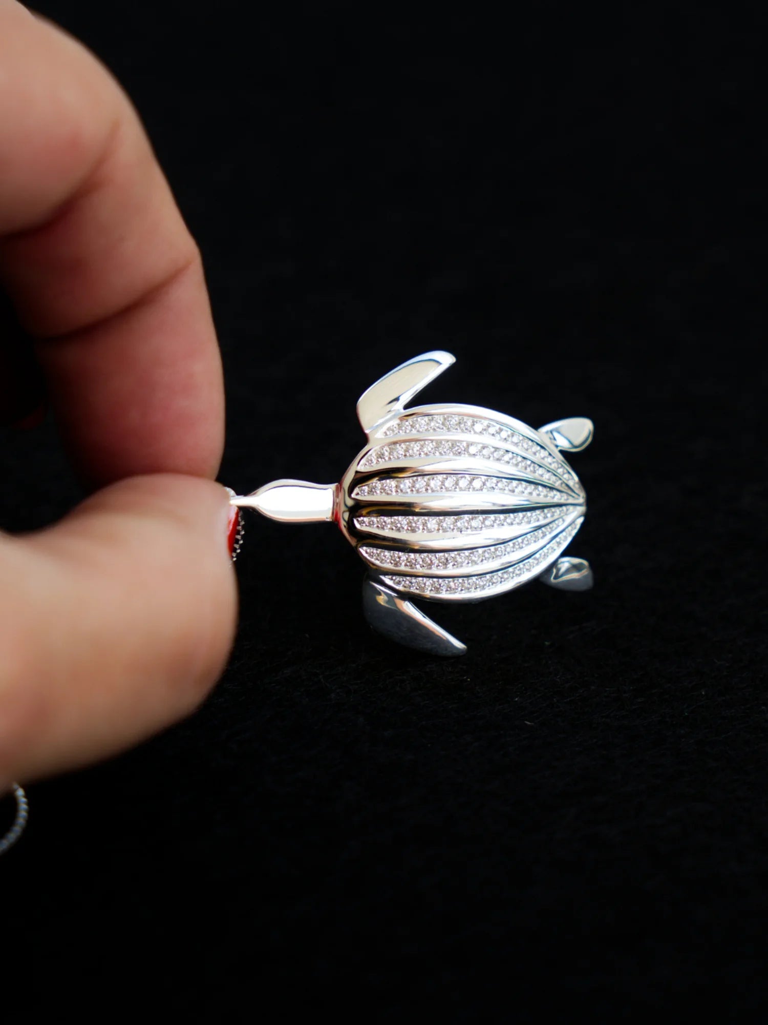 Le pendentif Totem Luth tenu entre les doigts, ses rangées de diamants en gros plan, de la collection Totem Luth | Honu