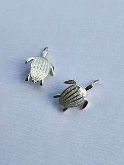 Les boucles d'oreilles Totem Luth, diamants incolores sur argent massif, la paire posée en biais, les sept carènes détaillées | Honu