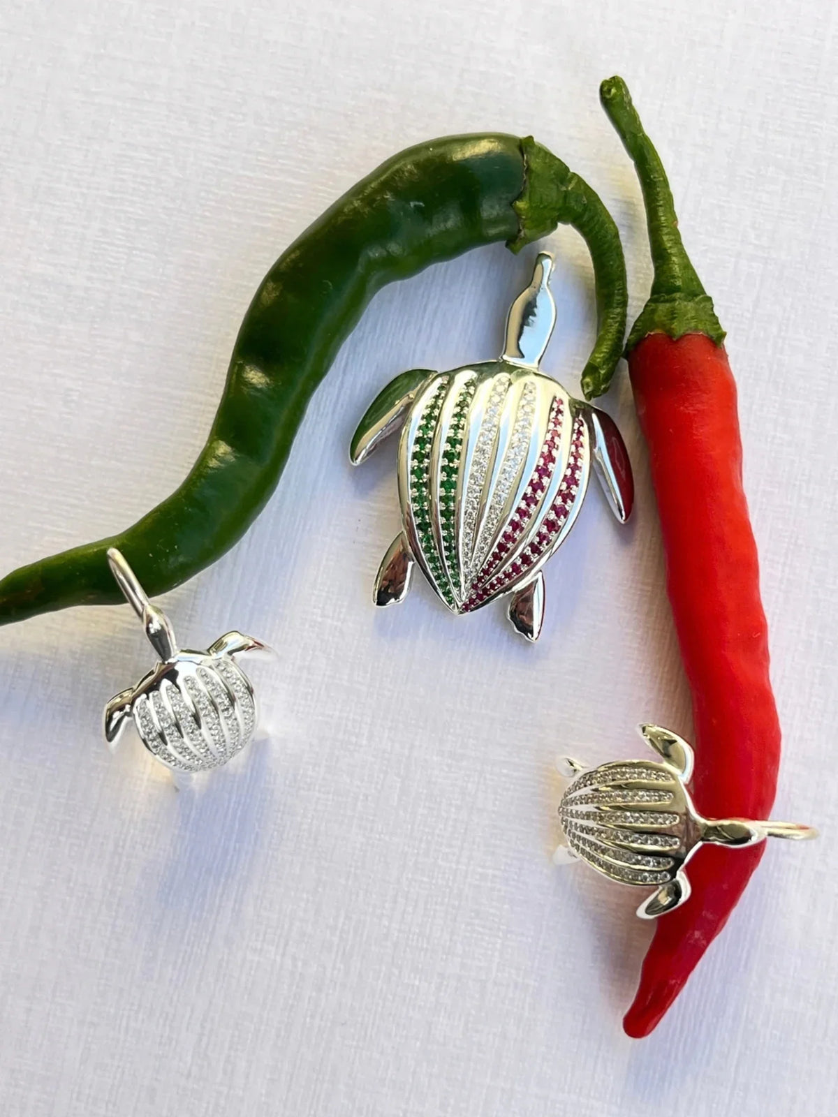 Les boucles d'oreilles Totem Luth, diamants incolores sur argent massif, en gros plan avec le pendentif Totem Luth Italia et deux piments vert et rouge | Honu