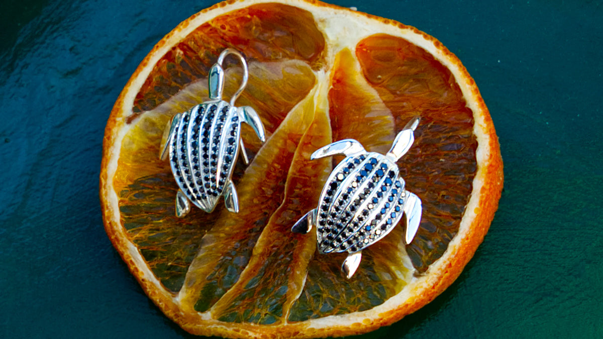 Les boucles d'oreilles Totem Luth, diamants noirs sur argent massif, sur une rondelle d'orange séchée, panoramique sur les carapaces pavées | Honu