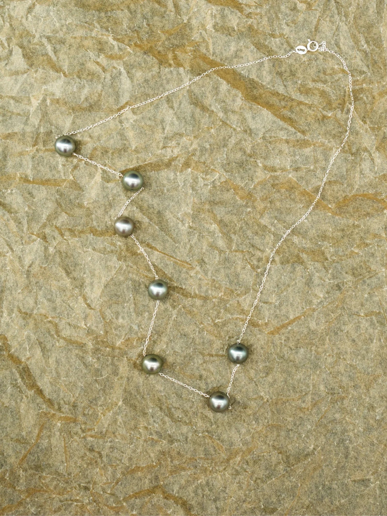 Le collier Émergence 21.98 déployé sur une pierre claire, ses sept perles de Tahiti, de la collection Instinct | Honu