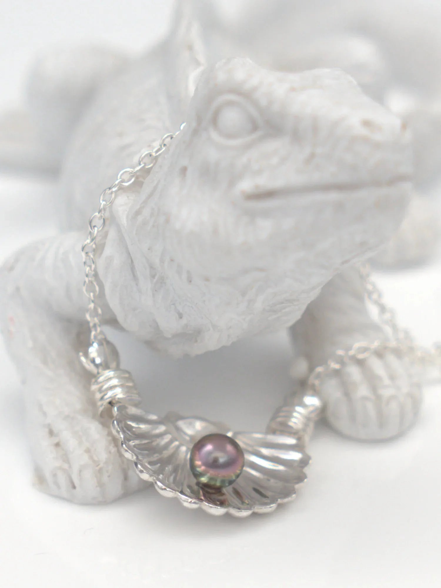 Collier en argent massif 950 avec pendentif coquillage et perle de Tahiti foncée, posé sur une statue blanche.