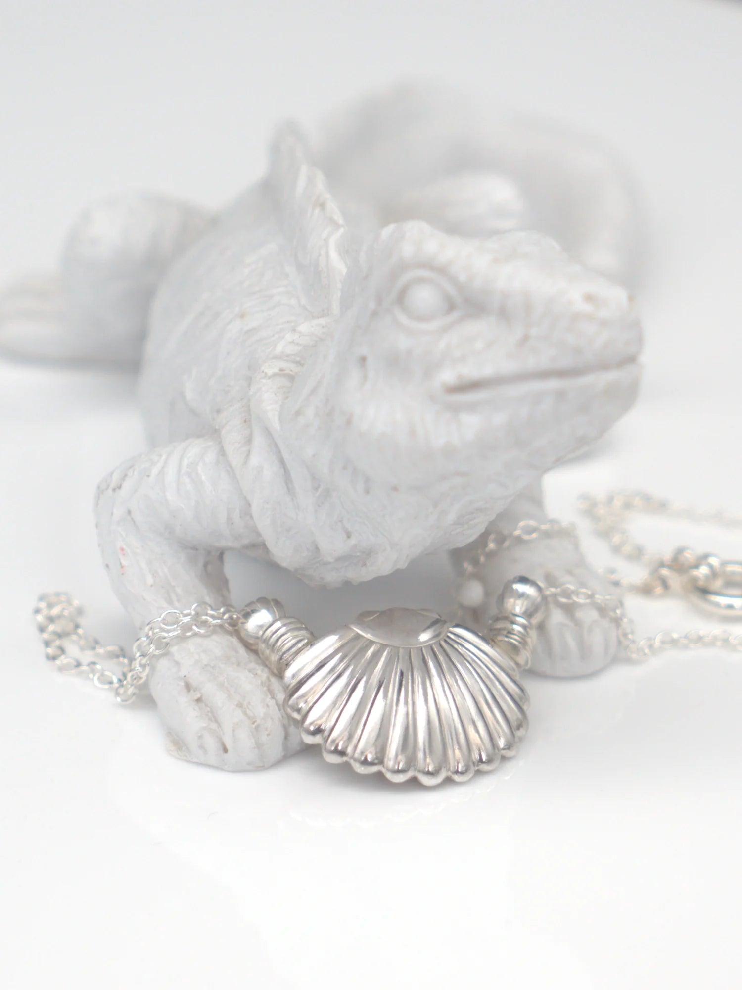 Collier en argent massif 950 avec pendentif coquillage, posé devant une figurine d'iguane blanche.