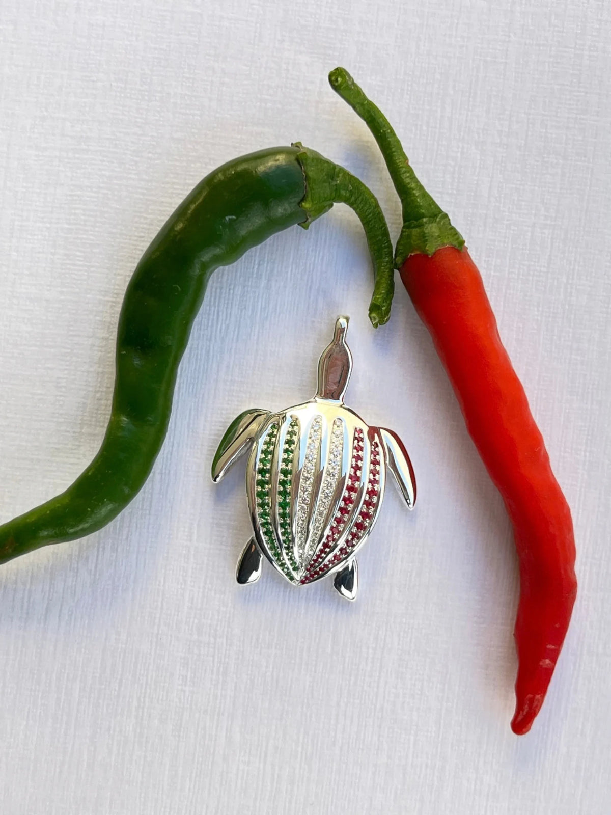 Le pendentif Totem Luth Italia, tsavorites, diamants et rubis sur argent massif, au centre, encadré d'un piment vert et d'un piment rouge | Honu