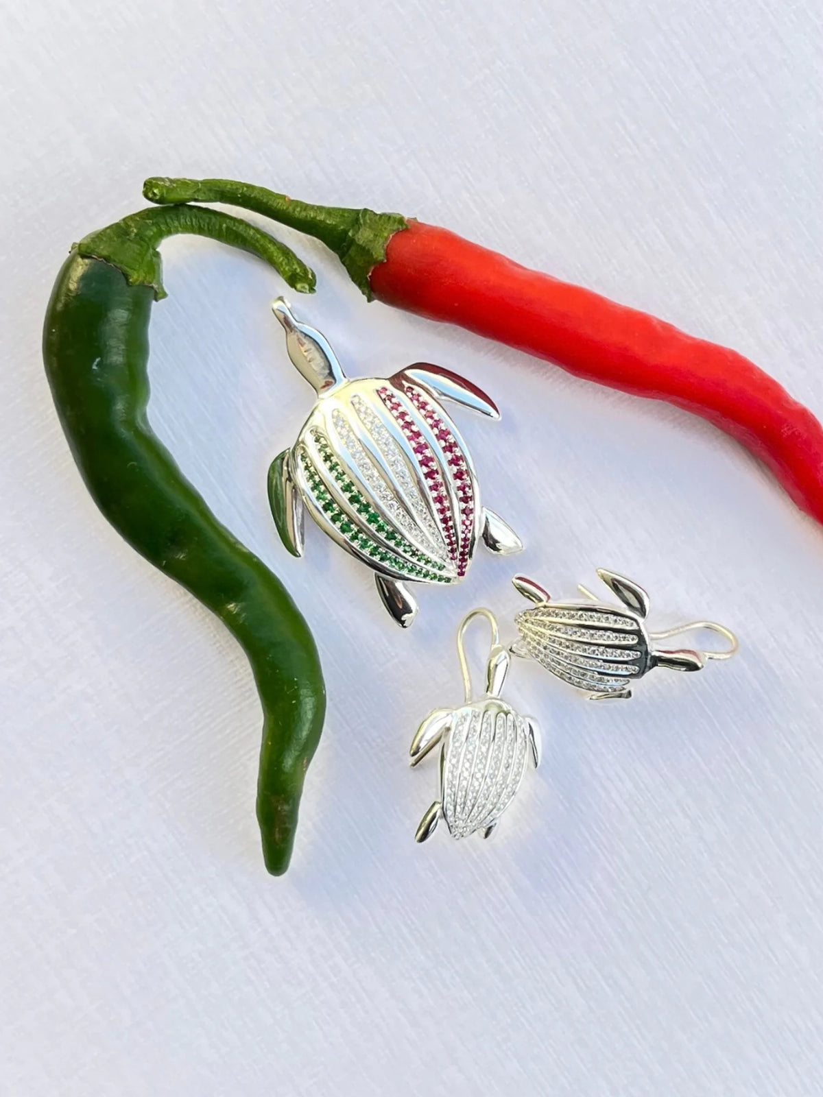 Le pendentif Totem Luth Italia, tsavorites, diamants et rubis sur argent massif, avec une paire de boucles d'oreilles Totem Luth, entre piments vert et rouge | Honu