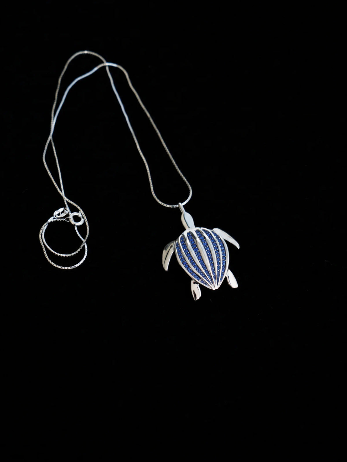 Le pendentif Totem Luth, saphirs bleus sur argent massif, présenté avec sa chaîne lovée sur fond noir | Honu