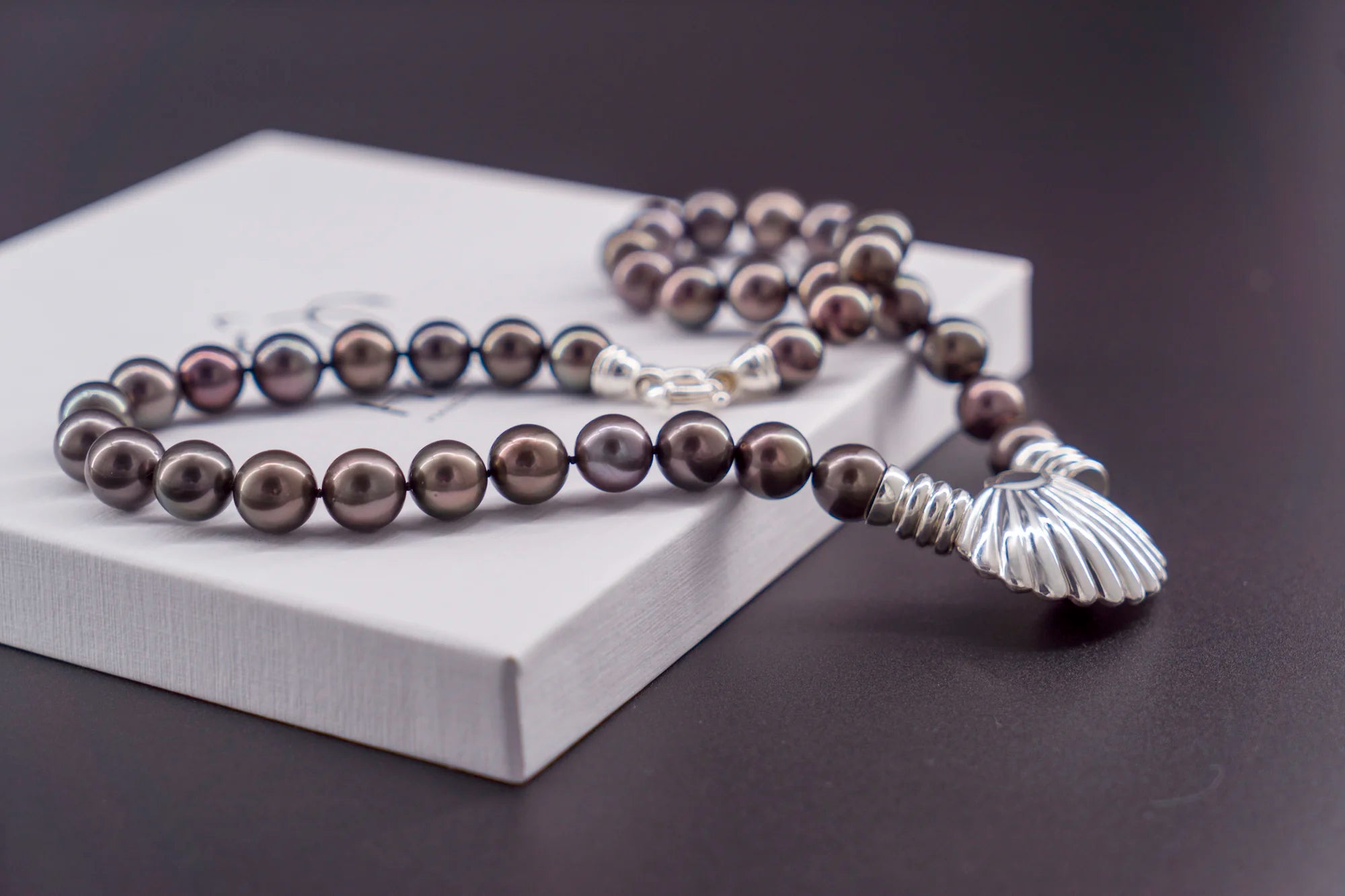 Collier artisanal en argent massif 950 et perles de Tahiti sombres, posé sur une boîte blanche.
