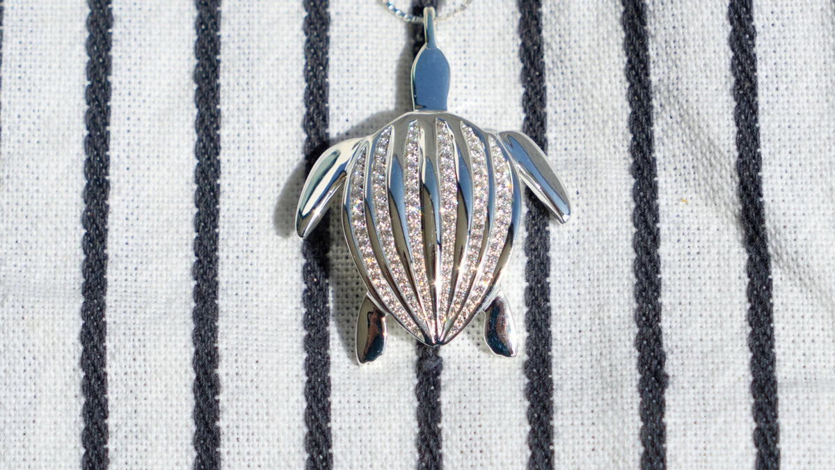 Le pendentif Totem Luth et ses rangées de diamants, de la collection Totem Luth, posé sur un tissu rayé | Honu